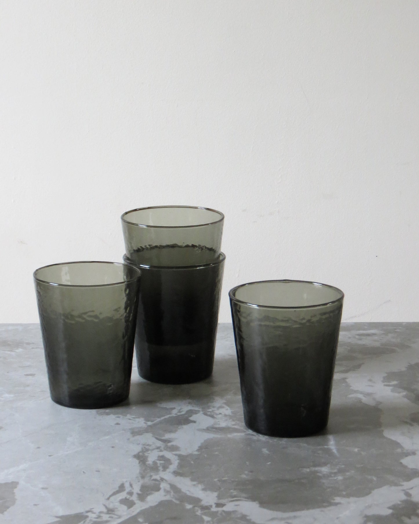 Set of four smoked glass tumblers on a textured surface.