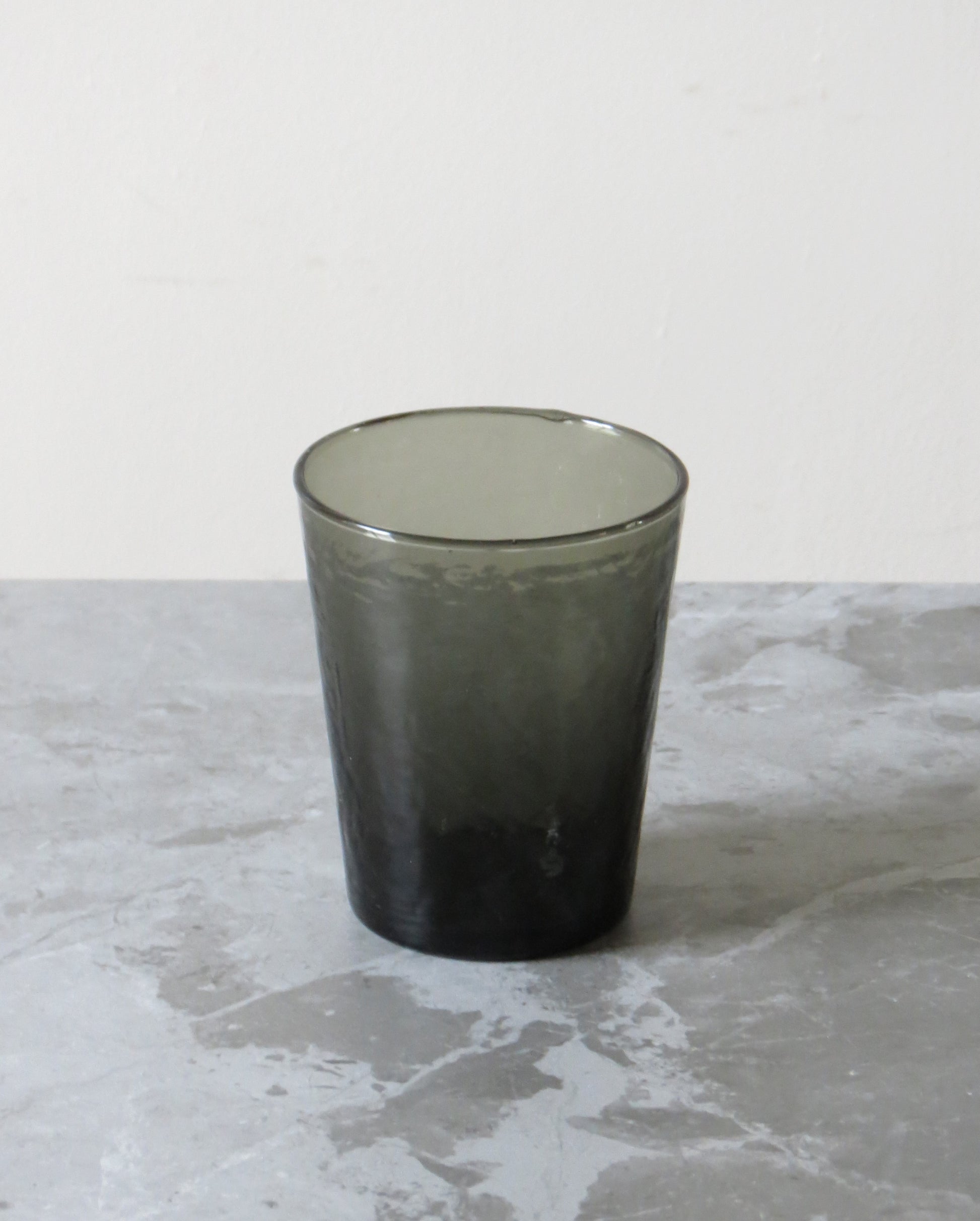 Dark glass tumbler on a textured grey surface.