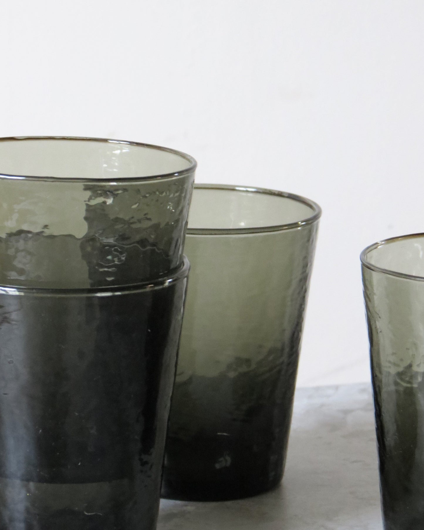 Three smoked glass tumblers on a white surface.