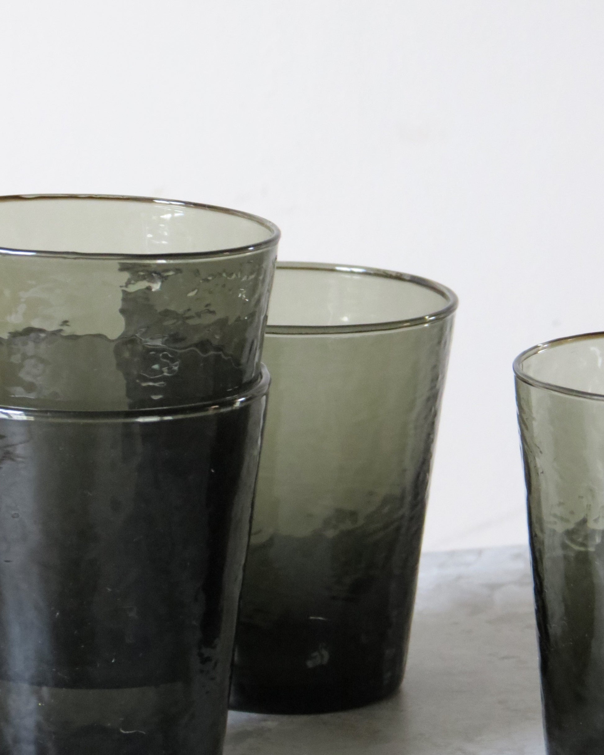 Three smoked glass tumblers on a white surface.