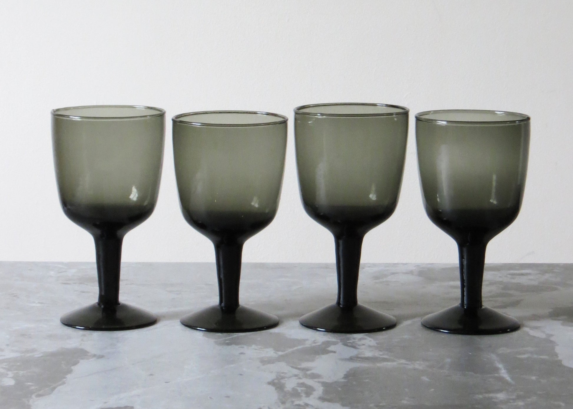 Four smoked glass wine glasses on a textured surface.