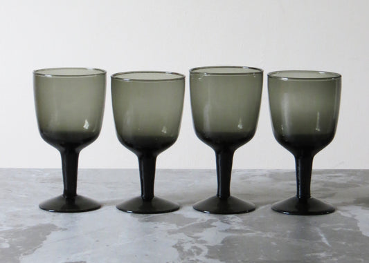 Four smoked glass wine glasses on a textured surface.