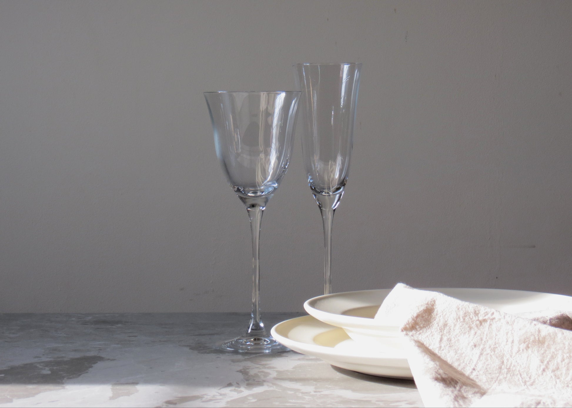 Two clear glass flutes on a marble surface with a neutral background