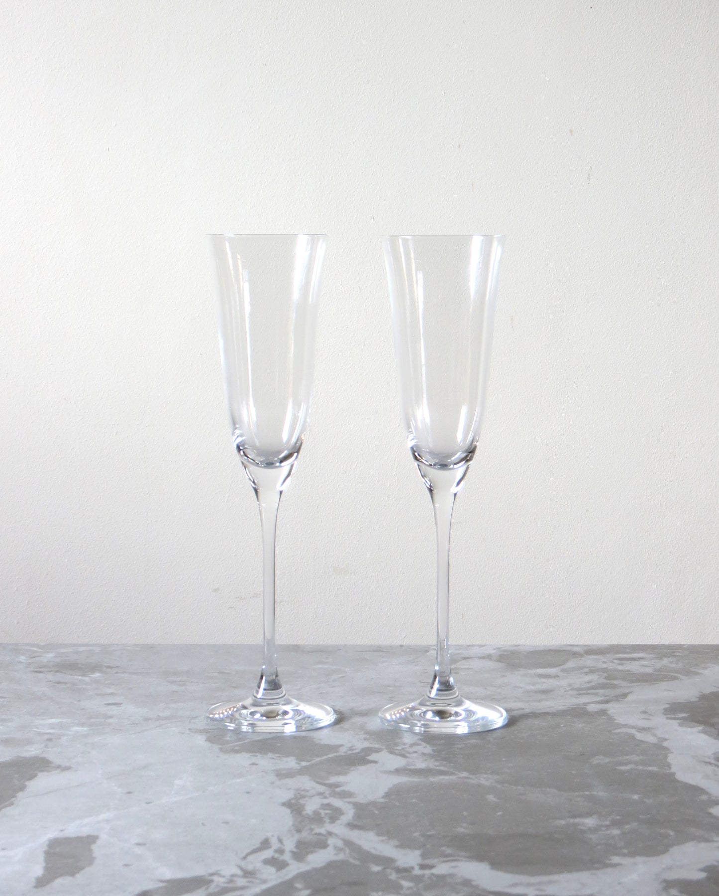 Two clear champagne flutes on a gray surface with a white background.