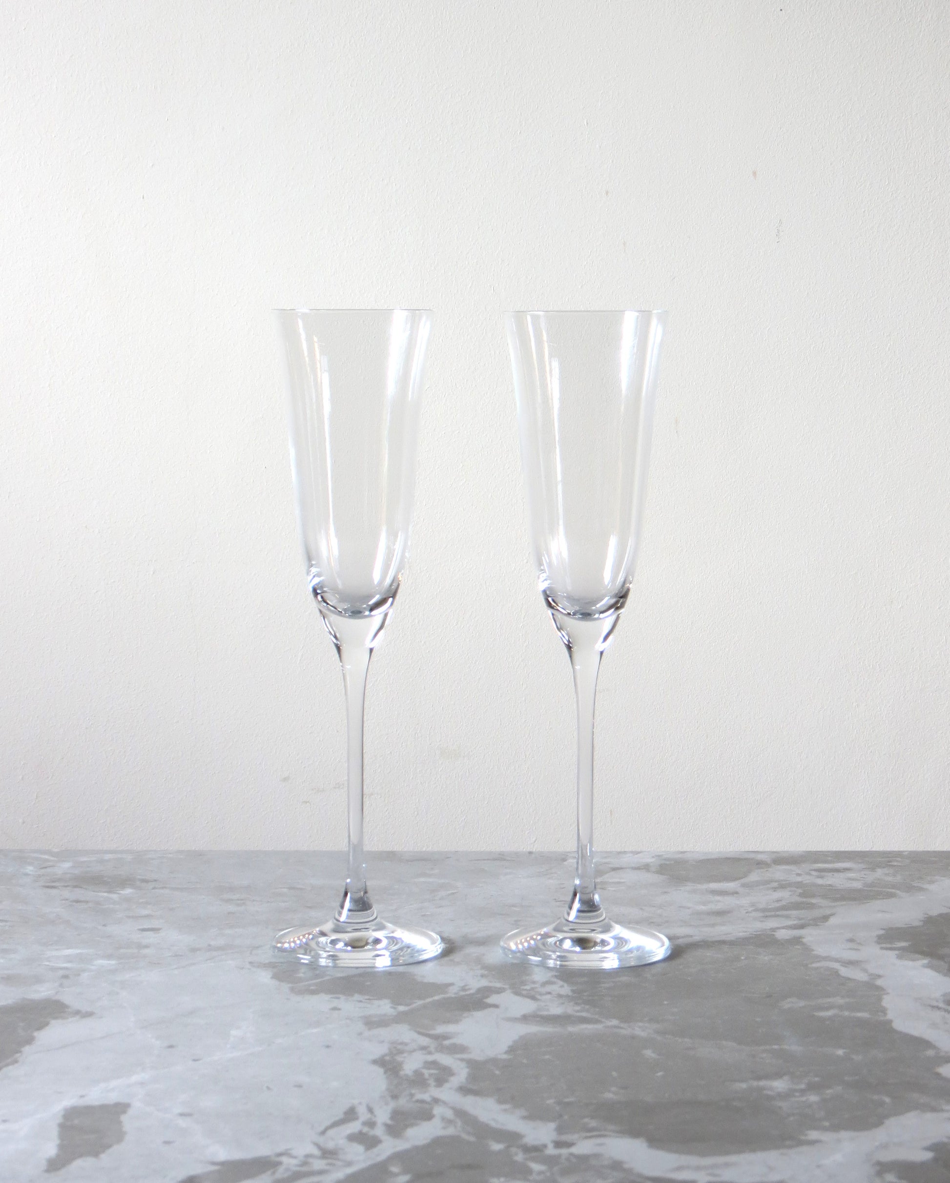 Two clear champagne flutes on a gray surface with a white background.