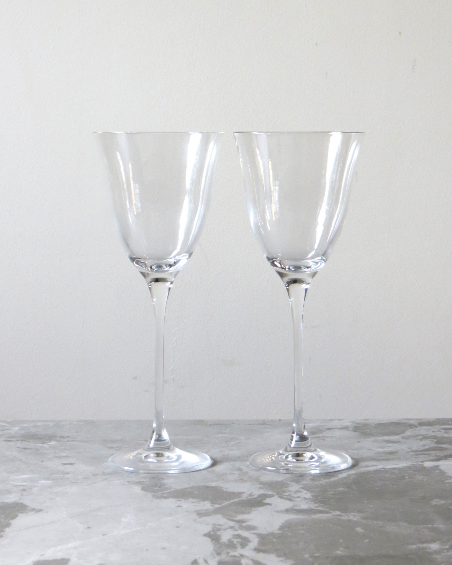 Two clear crystal tulip red wine glasses with long stems, empty and placed on a marble surface.