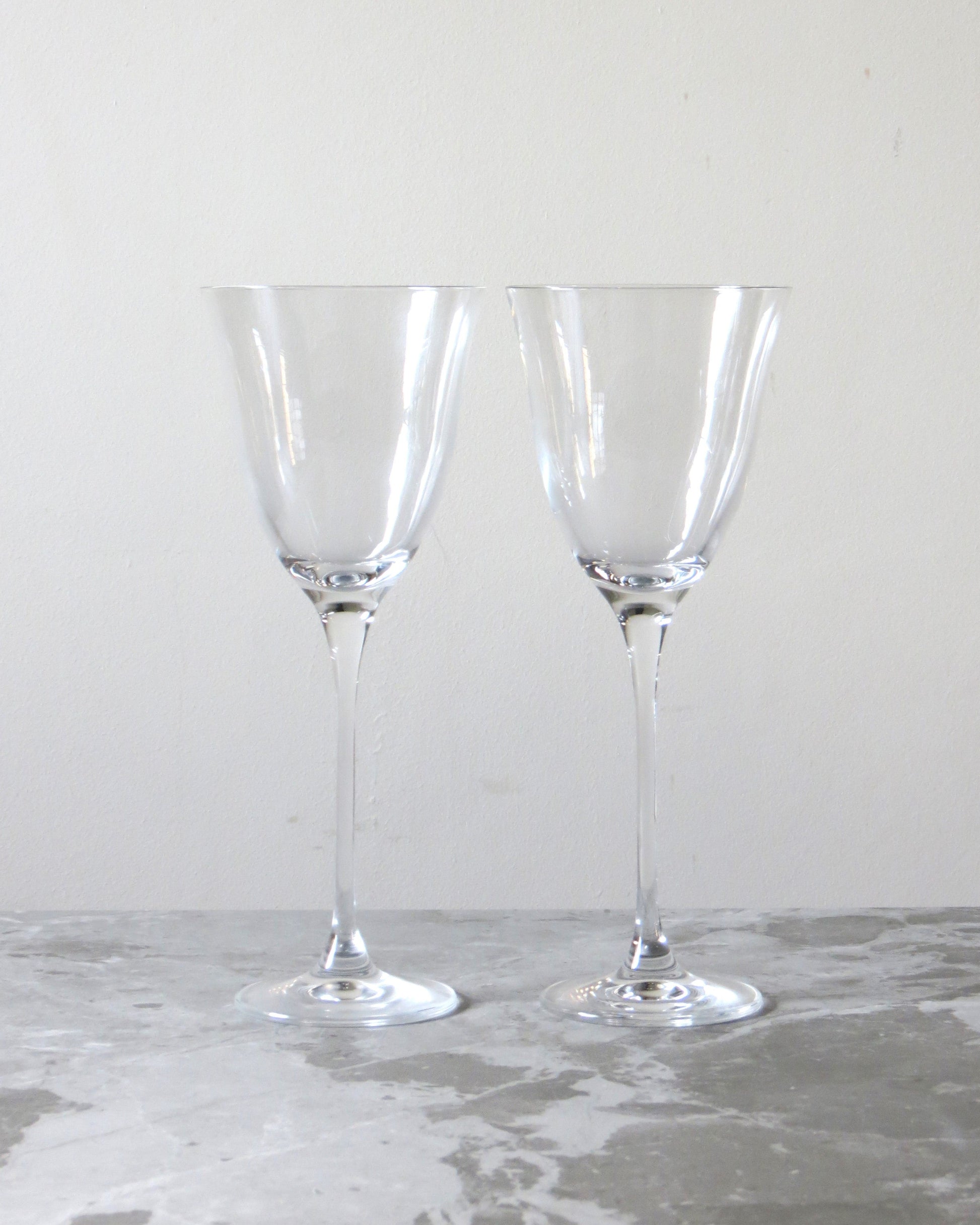 Two clear crystal tulip red wine glasses with long stems, empty and placed on a marble surface.
