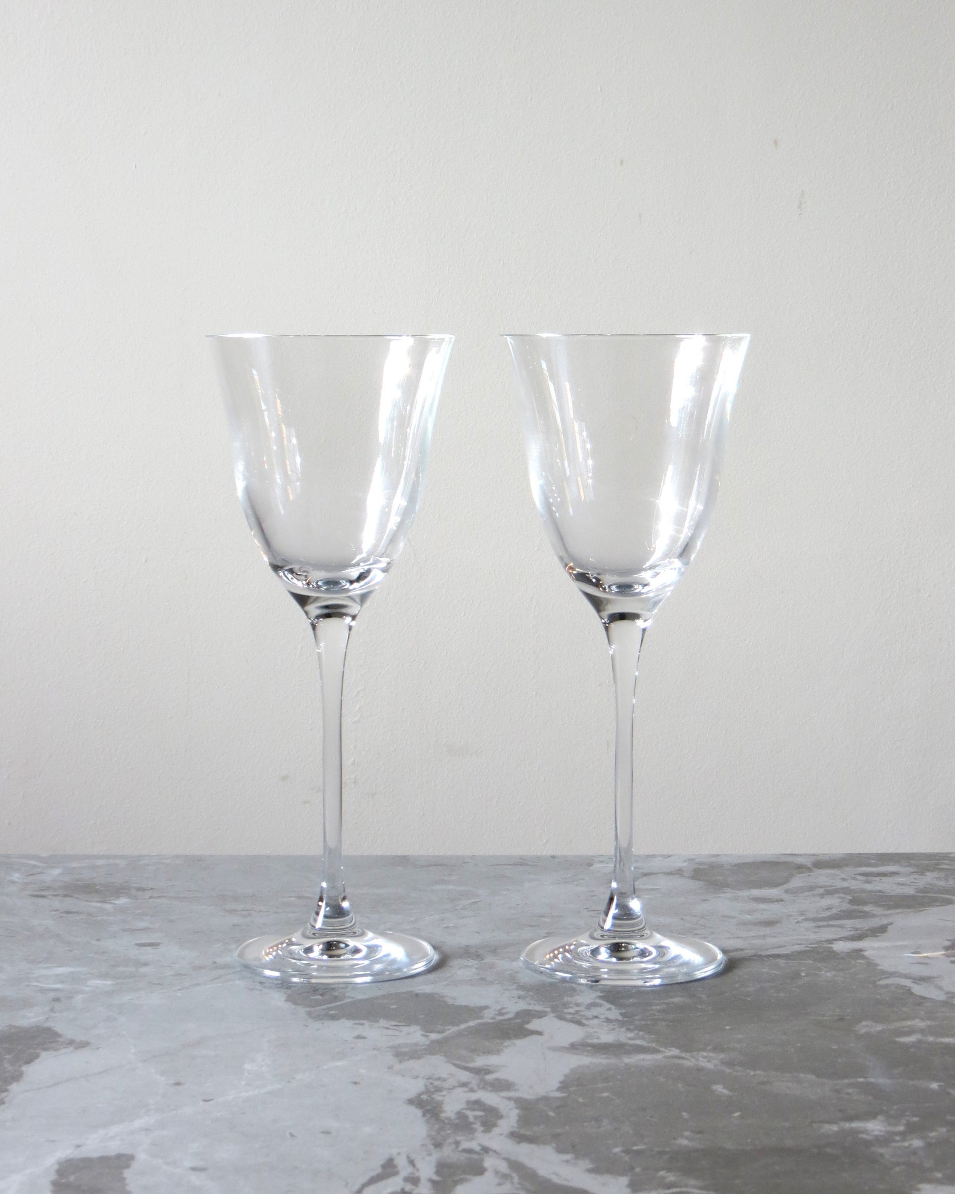 Two clear glass wine glasses on a gray surface with a white background.